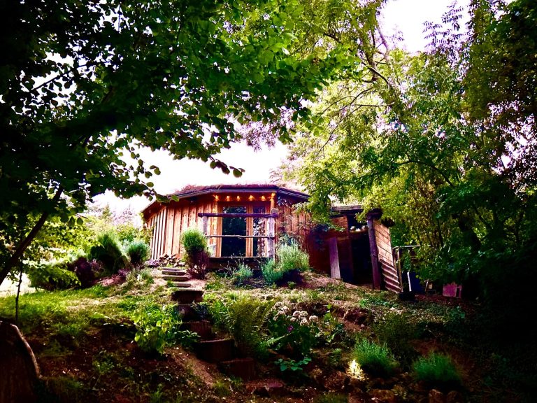 Maison en bois au milieu d'arbres, avec un jardin verdoyant et un chemin d'accès.